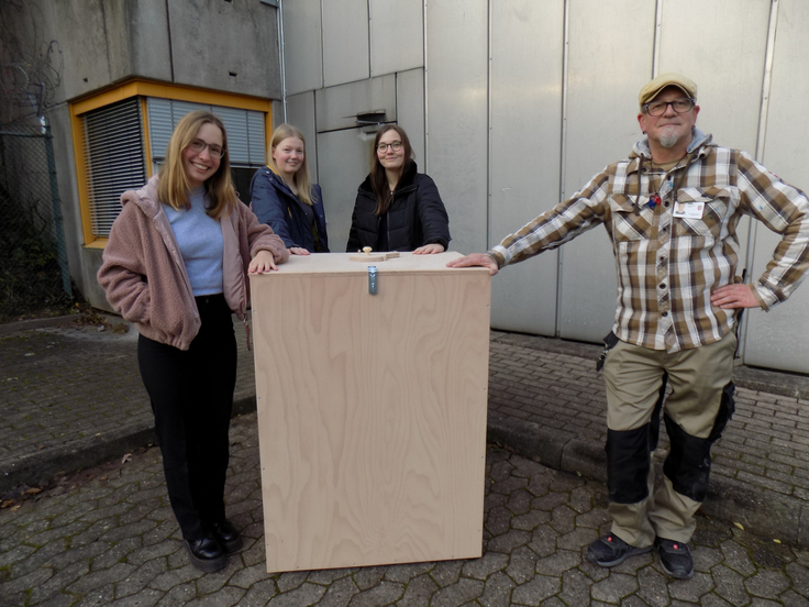 Drei externe Personen des Projekts und ein Bediensteter bei der Übergabe der Holzkiste